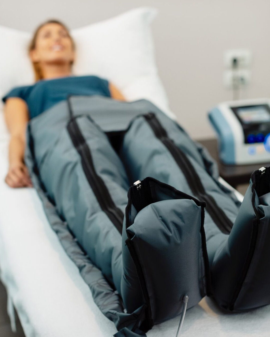 Mujer acostada en una camilla de tratamiento recibiendo terapia de compresión de piernas con presoterapia.